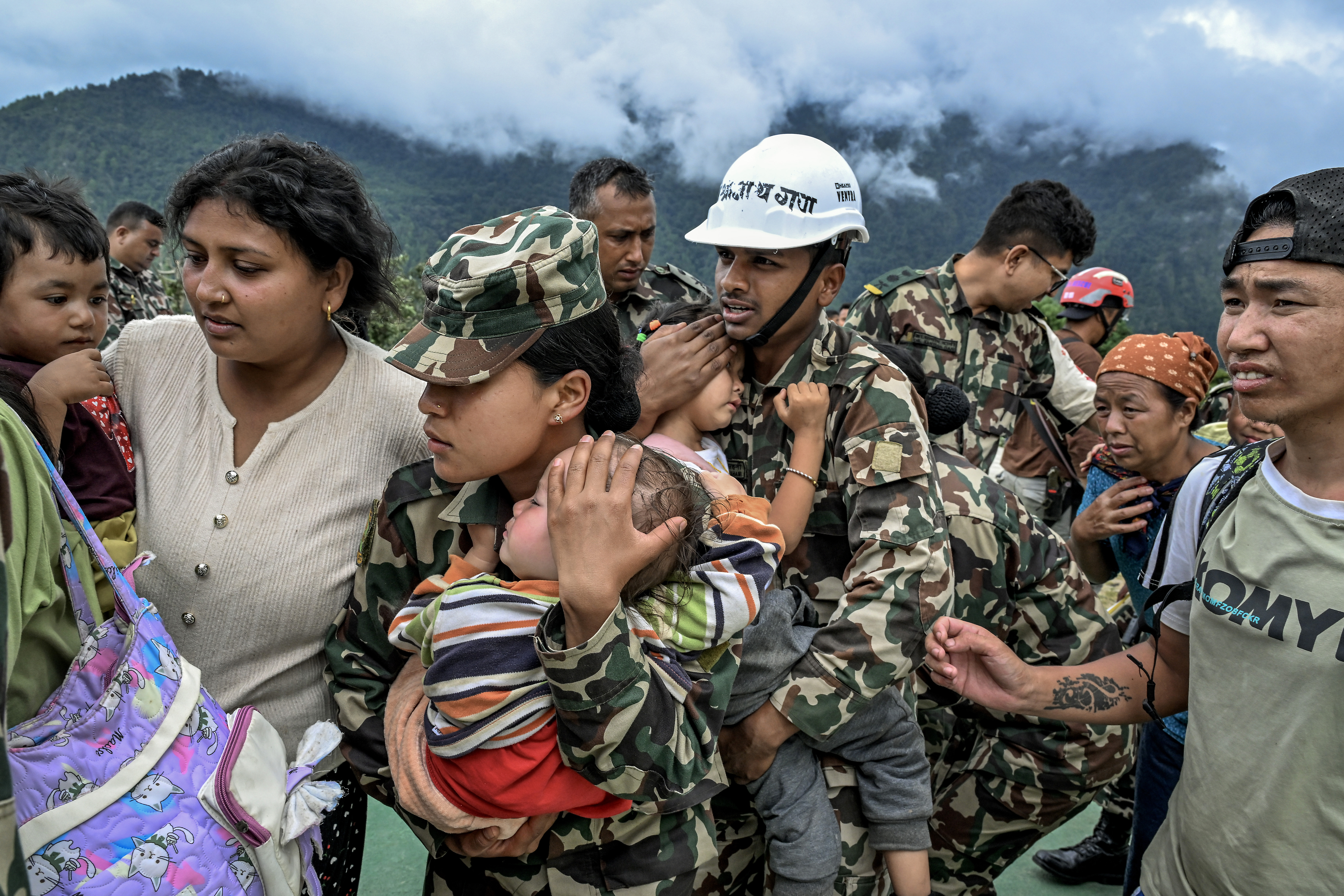 Children are carried to a rescue helicopter by military personnel in the disaster-stricken Rasuwa district near Nepal’s border with Tibet, on Thursday, Aug. 27, 2026. Emergency workers and helicopters scoured steep Himalayan valleys on Thursday in a desperate search for survivors after a torrent of water, mud and ice killed hundreds — and perhaps many more — as it swept through a river valley that runs through Tibet and Nepal. More than 1,400 people are still missing. (Atul Loke/The New York Times)