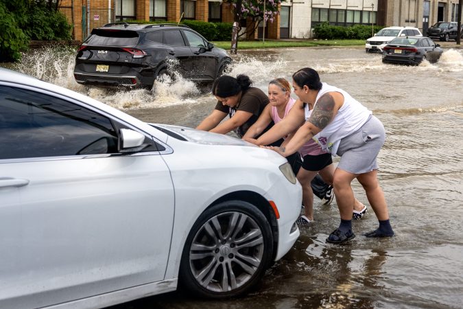 Husband Omar Marquez is behind the wheel as Angie Colon gets help from her mother, Maria Rodriguez, and daughter Leslie pushing their car after it stalled in high water on Ferry Avenue near the PATCO station on Monday.