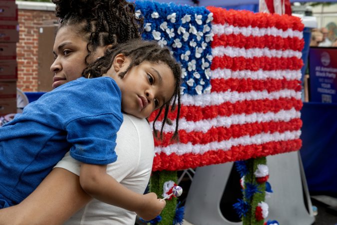 Ciera Brown carries her son, Asaad Neely, 3, as they march in the second annual Red, White, & Blue To-Do parade Wednesday, Jul, 2, 2025, along with whimsical red wagon floats, marching bands, John Adams and Ben Franklin, and representatives from over twenty groups across Philadelphia’s Historic District. The event commemorates a day of “pomp and parade,” as declared by John Adams in 1776. He believed Independence Day would be celebrated on the 2nd - when the Continental Congress officially voted for independence - not two days later when he, John Hancock (and 54 others) signed their document.
